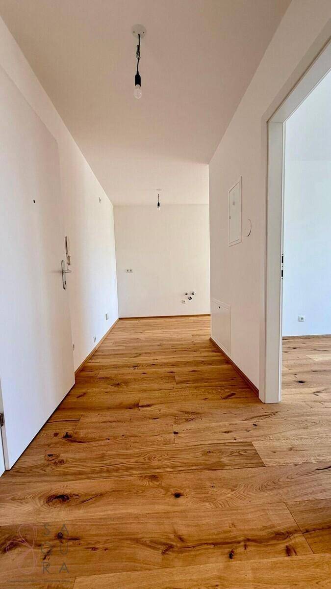 Langer, heller Flur mit Holzboden und weißen Wänden in einem modernen Gebäude.