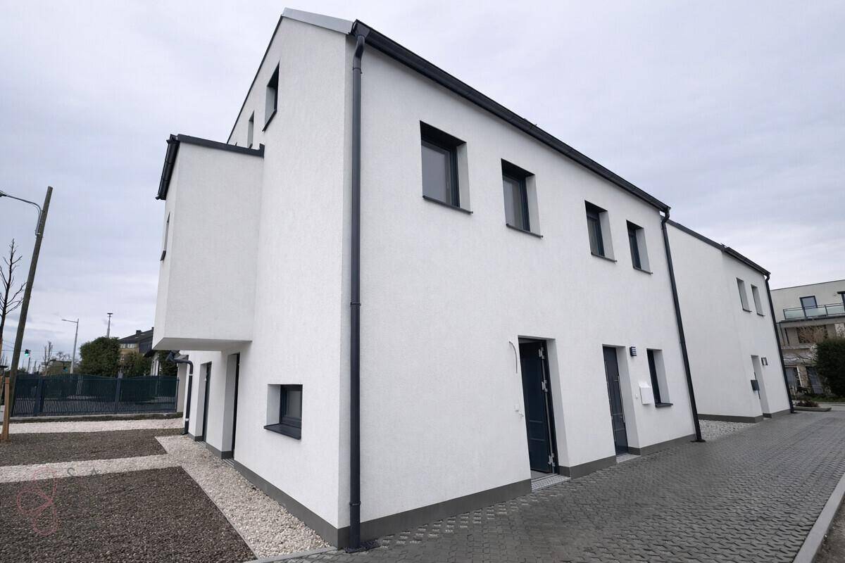 Seitenansicht eines neu gebauten Reihenhauses mit weißer Fassade und dunklen Fenstern.