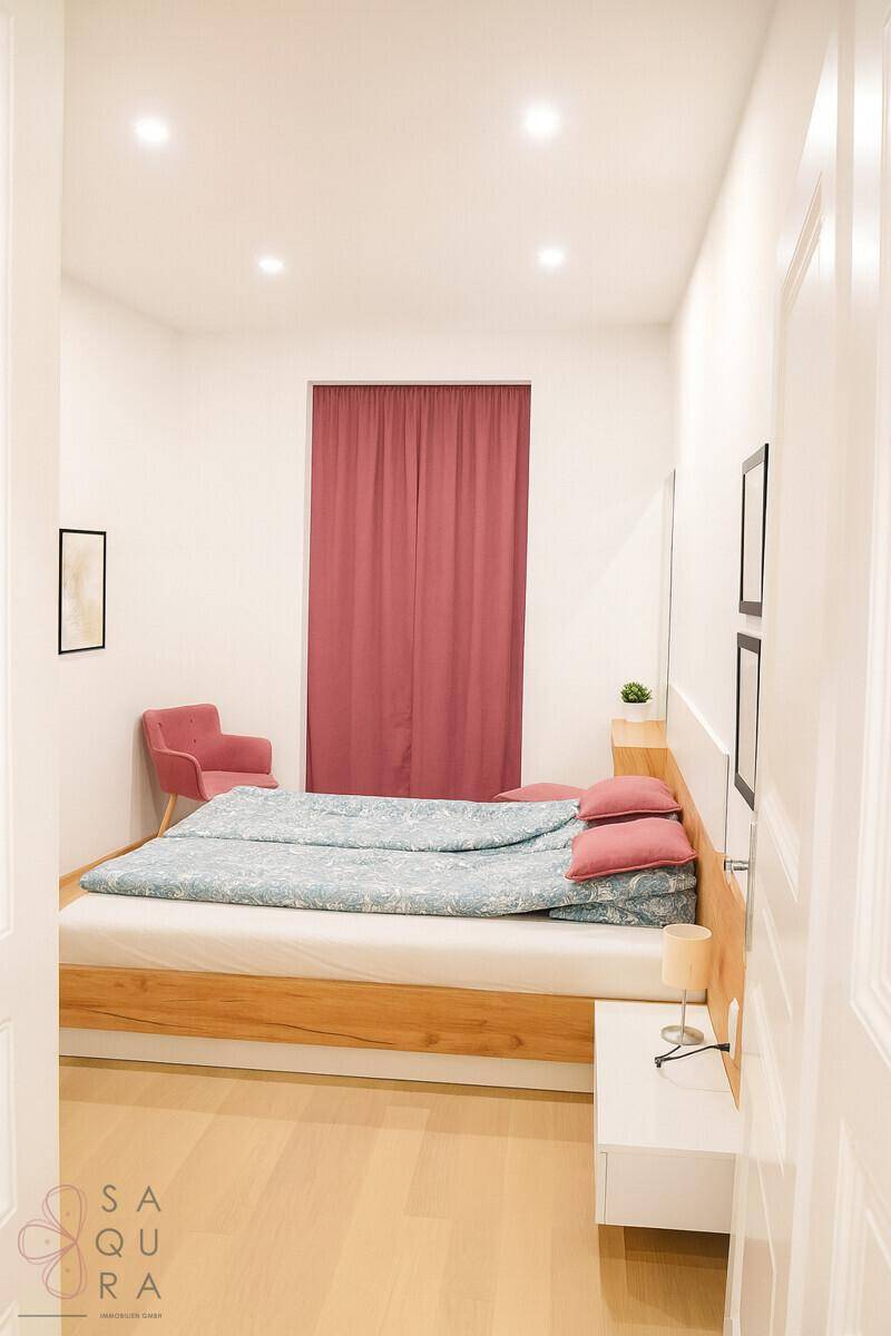 Schlafzimmer mit Doppelbett, Holzrahmen und roten Vorhängen, helle Wände und Parkettboden.