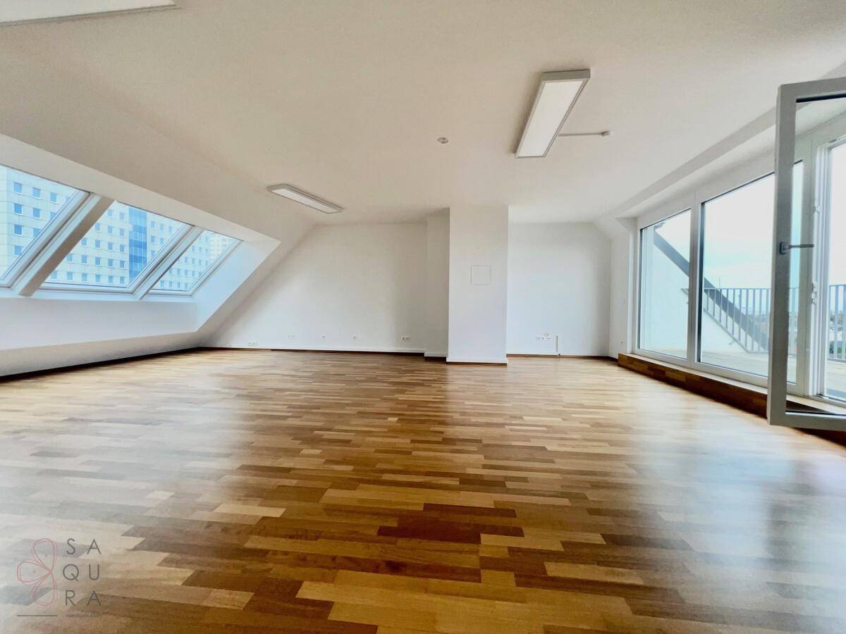 Geräumiger, heller Wohnraum mit Holzboden, Dachschrägen und großen Dachfenstern, die viel Licht hereinlassen.