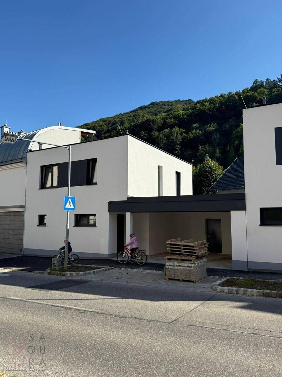 Moderne Reihenhäuser mit weißer Fassade und integriertem Carport an einer ruhigen Wohnstraße.