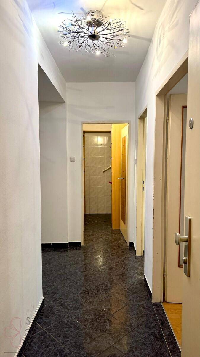 Leerer Flur mit dunklem Fliesenboden und einer auffälligen Deckenleuchte, die den Raum beleuchtet.