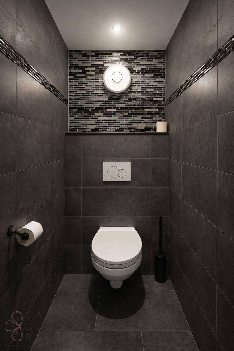Modernes Gäste-WC mit dunklen Fliesen, wandhängender Toilette und stilvoller Mosaikwand.