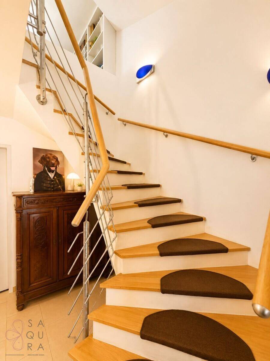 Holztreppe mit Edelstahlgeländer und antikem Schrank im Treppenbereich.