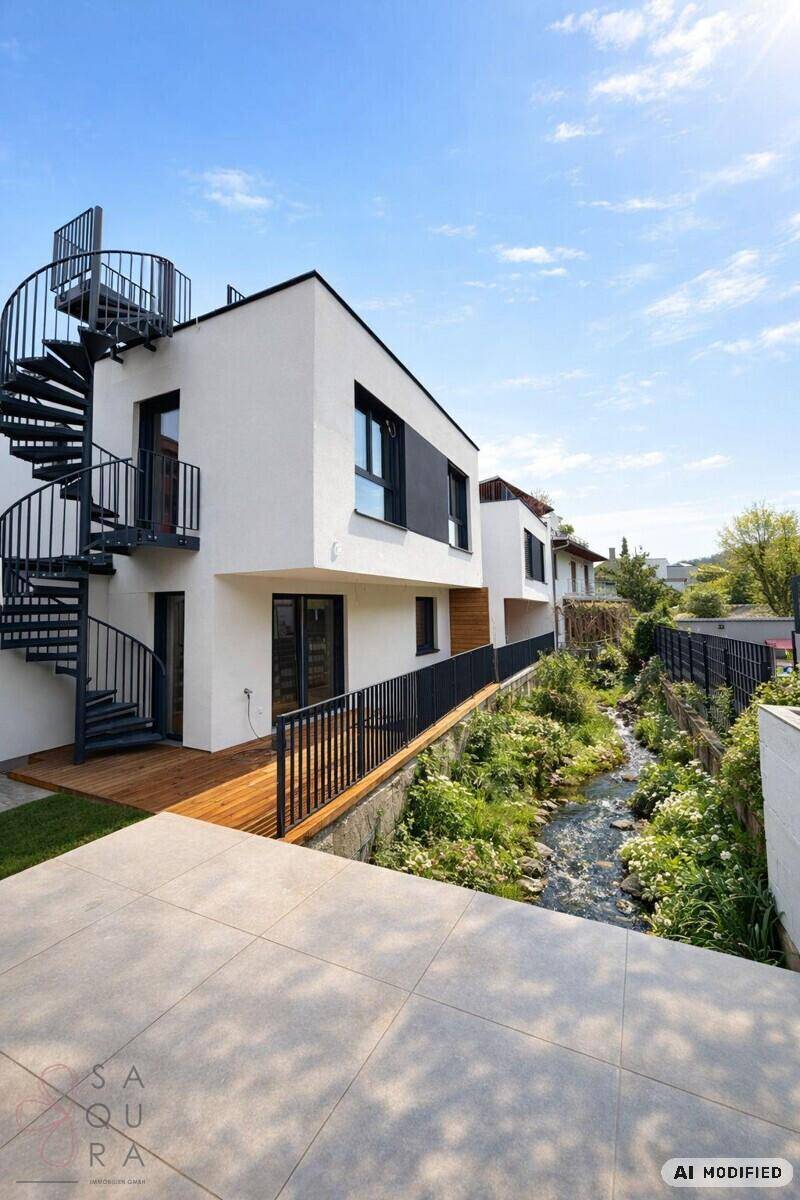 Außenansicht eines modernen Hauses mit spiralförmiger Außentreppe und Terrassenbereich am Bach.