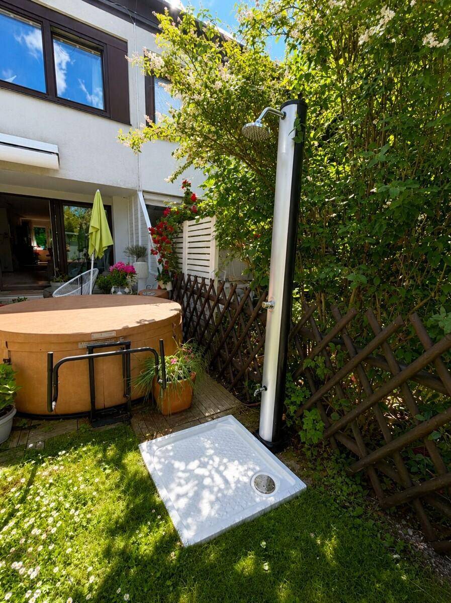 Grüner Gartenbereich mit Außendusche und einem einladenden Whirlpool.