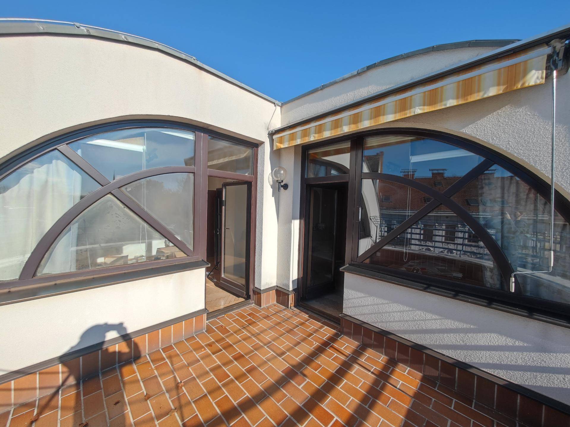 Kleiner Terrassenbereich mit Ziegelboden und markanten Rundbogenfenstern, bietet Zugang zu Innenräumen.