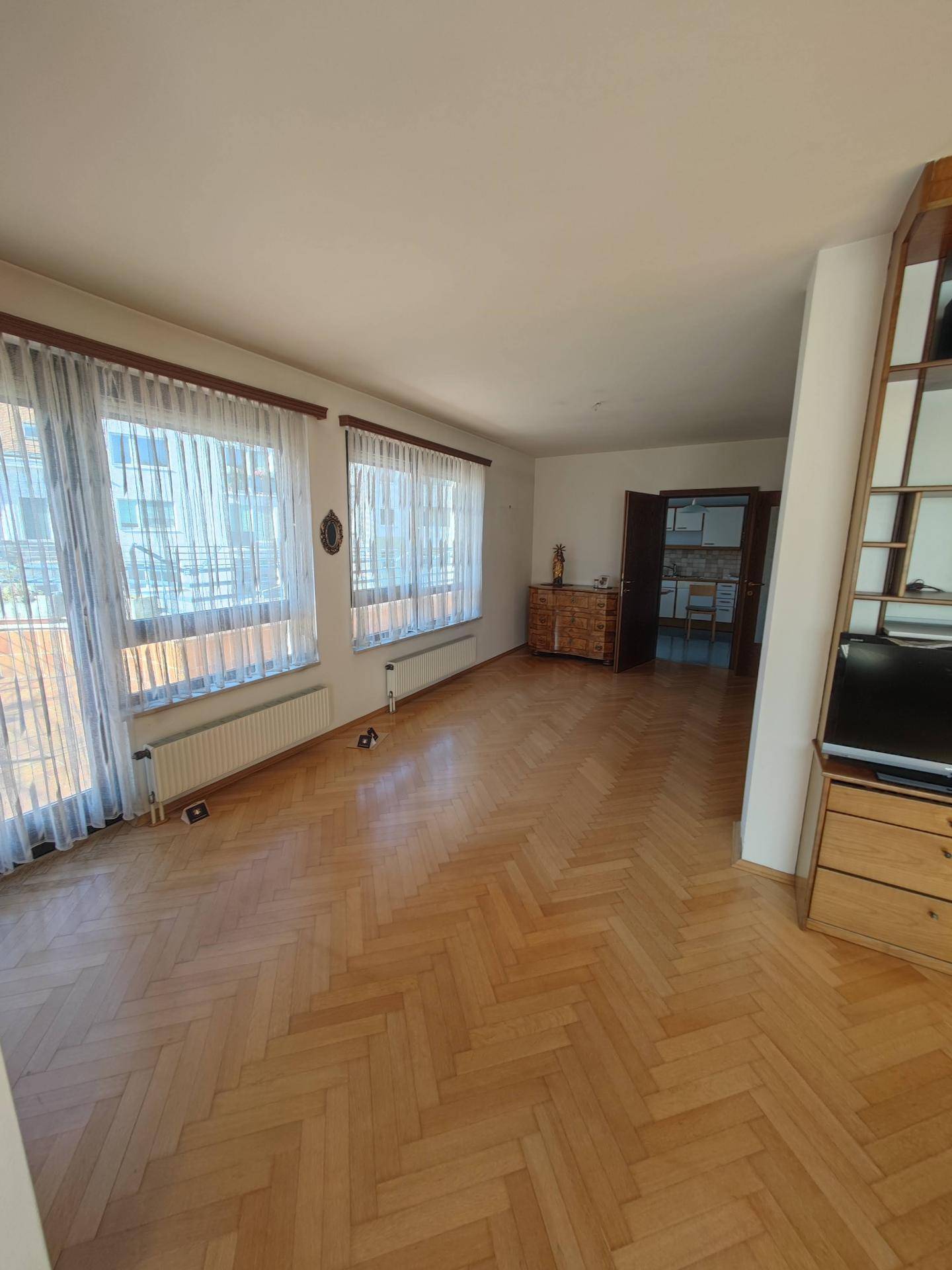 Großzügiges Wohnzimmer mit Fischgrätparkett und Zugang zur Terrasse, lichtdurchflutet und geräumig.