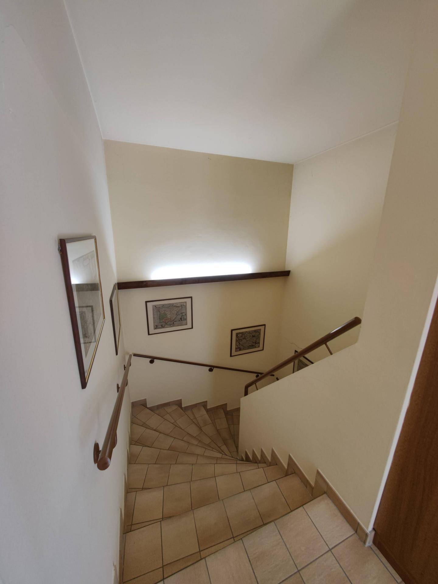 Geschwungene Treppe mit Fliesenboden und Holzgeländer, verbindet die verschiedenen Ebenen des Hauses.