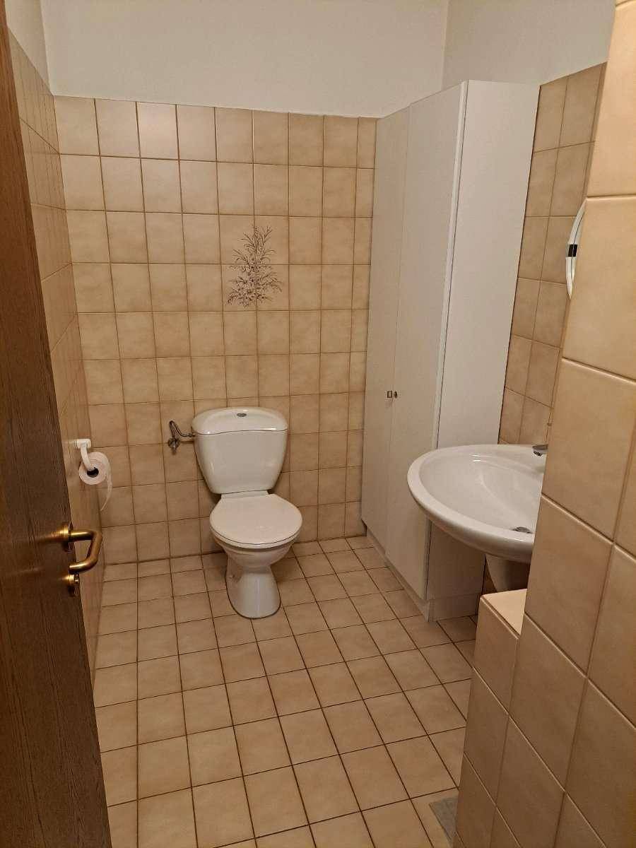 Kleines Gäste-WC mit beigefarbenen Fliesen, Toilette und Waschbecken, funktional und sauber.
