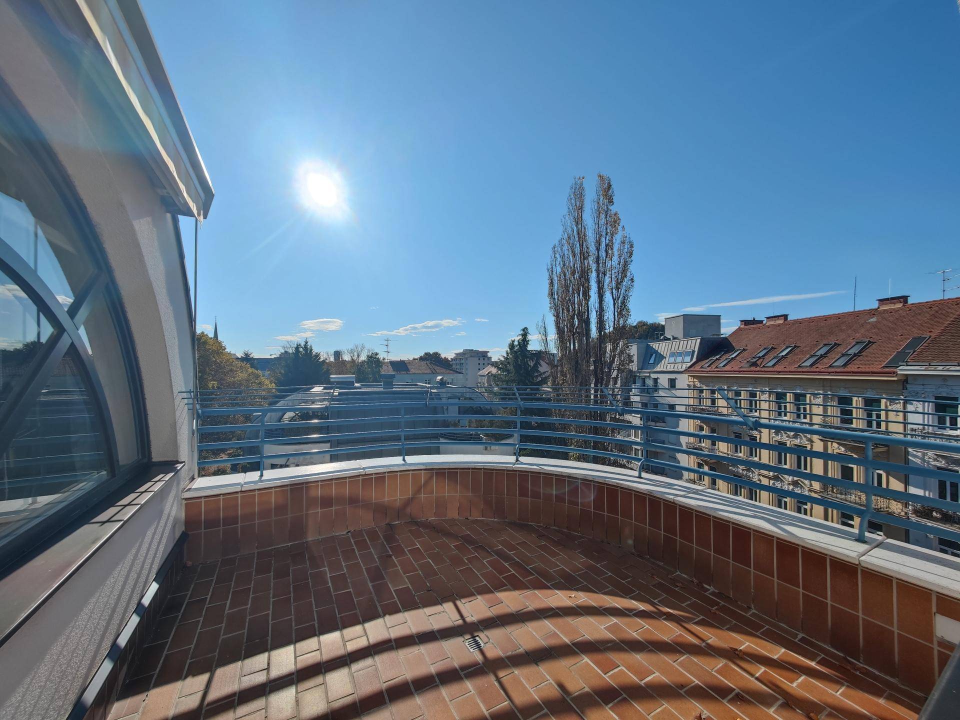 Sonnige Dachterrasse mit blauer Balustrade und weitem Blick über die Stadtlandschaft.