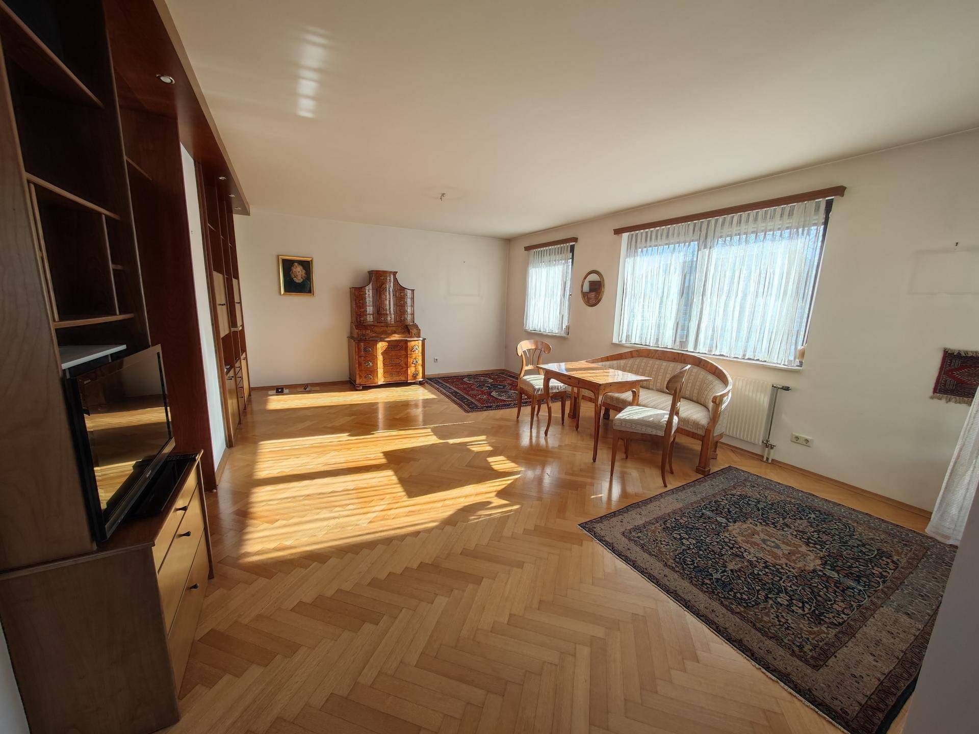 Geräumiger Wohn-Essbereich mit Fischgrätparkett und viel Tageslicht, eingerichtet mit klassischen Möbeln.