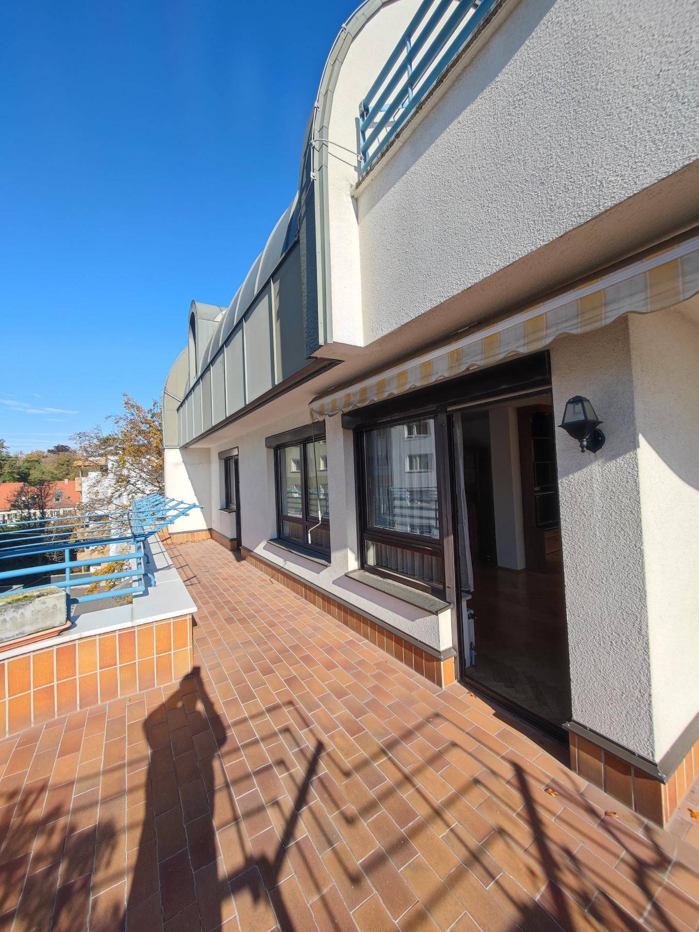 Sonnige Terrasse mit Ziegelboden und Zugang zum Innenbereich, umgeben von einer blauen Balustrade.