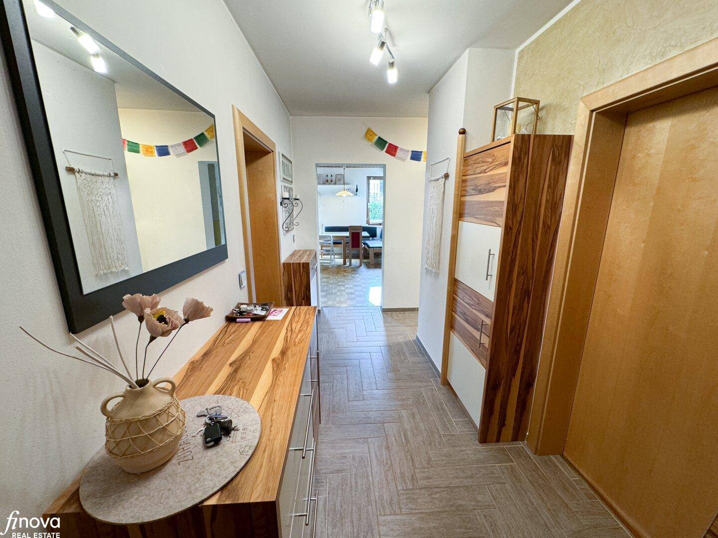 Heller Flur mit Holzmöbeln, Spiegel und Blick in den Essbereich, ausgestattet mit Fliesenboden.