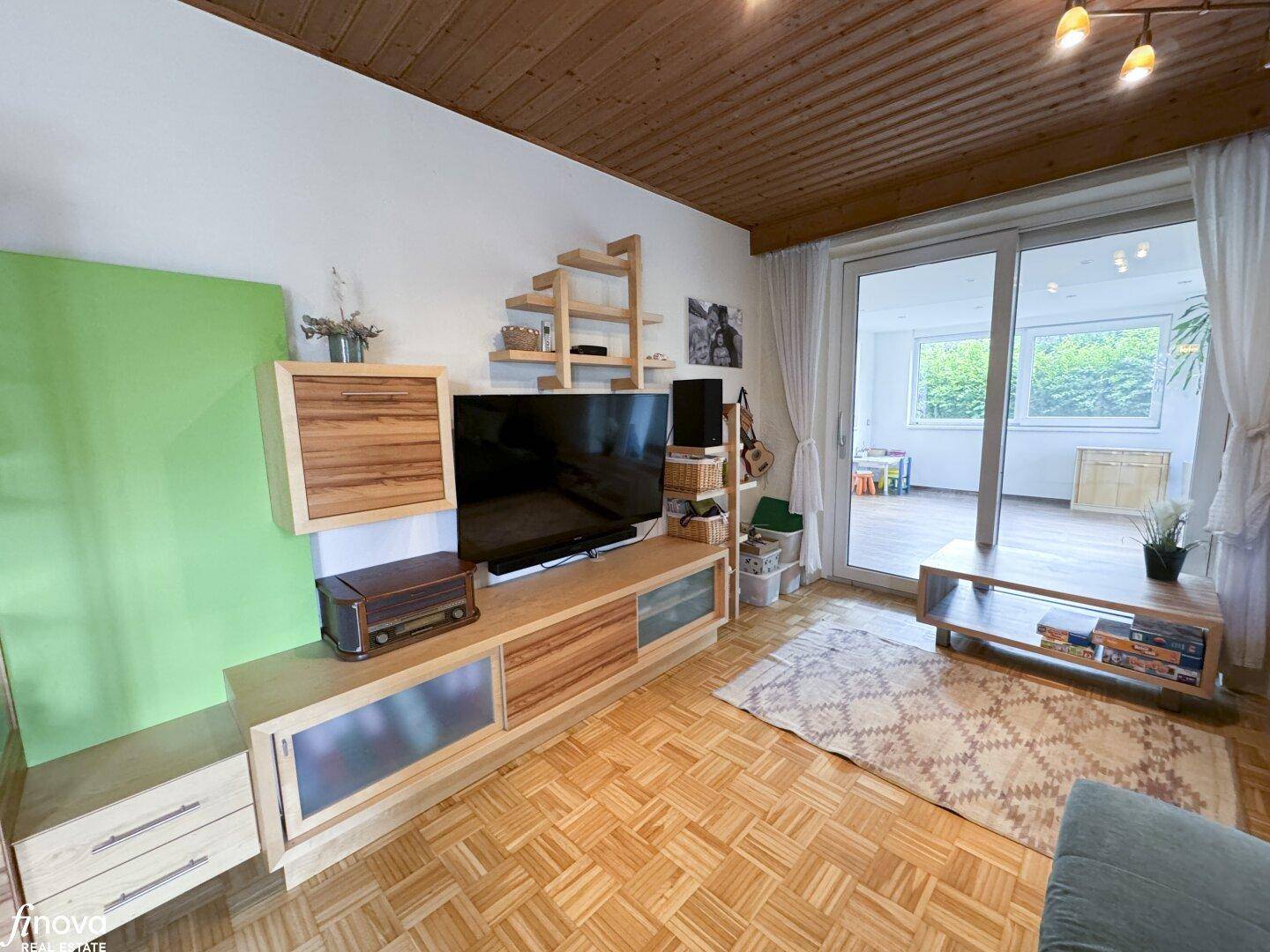 Wohnzimmer mit TV-Möbeln, Parkettboden und Schiebetür zur Terrasse, bietet viel Tageslicht.