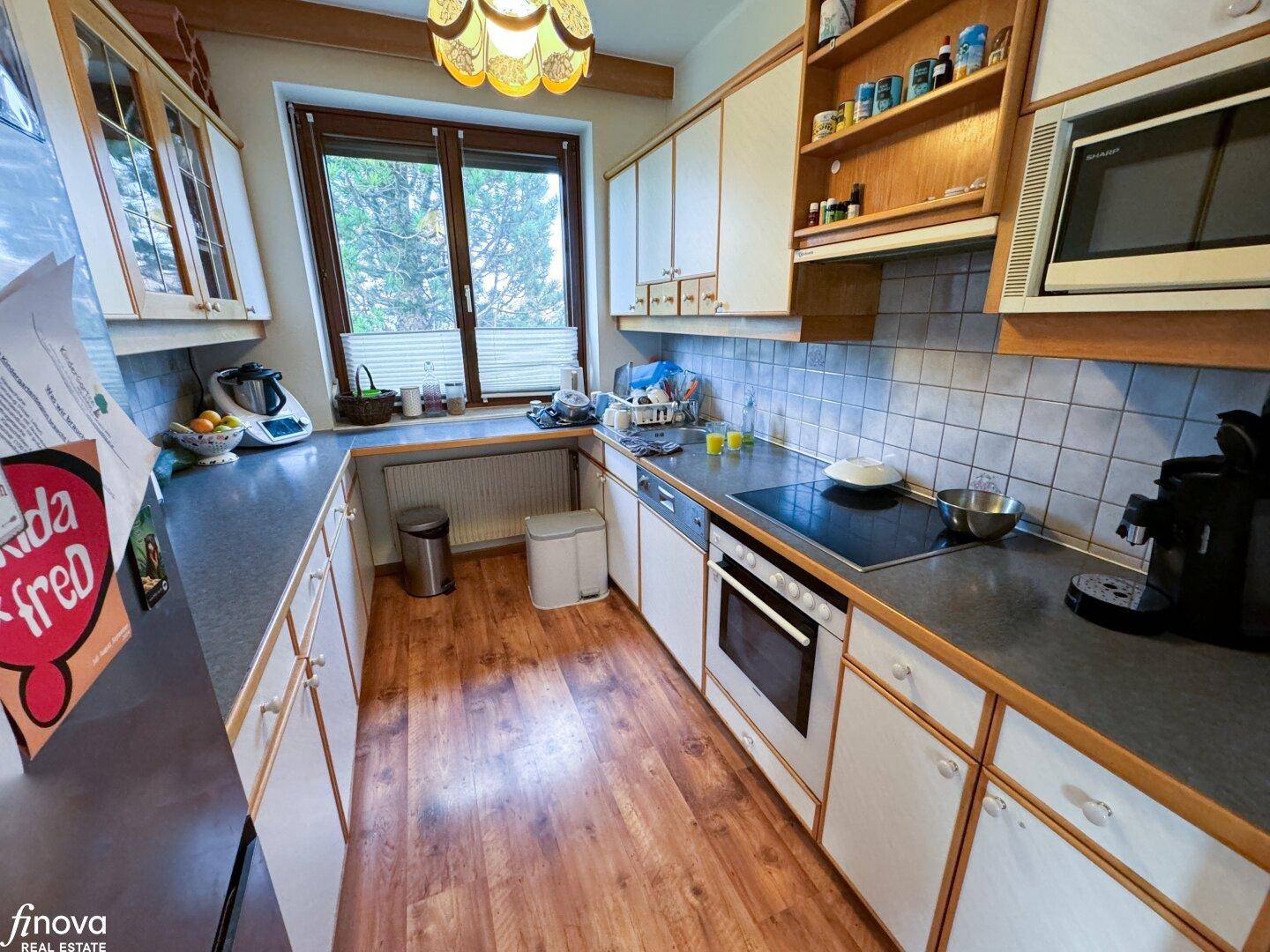 Funktionale Küche mit weißen Schränken, Holzfußboden und Fenster, inklusive moderner Geräte.