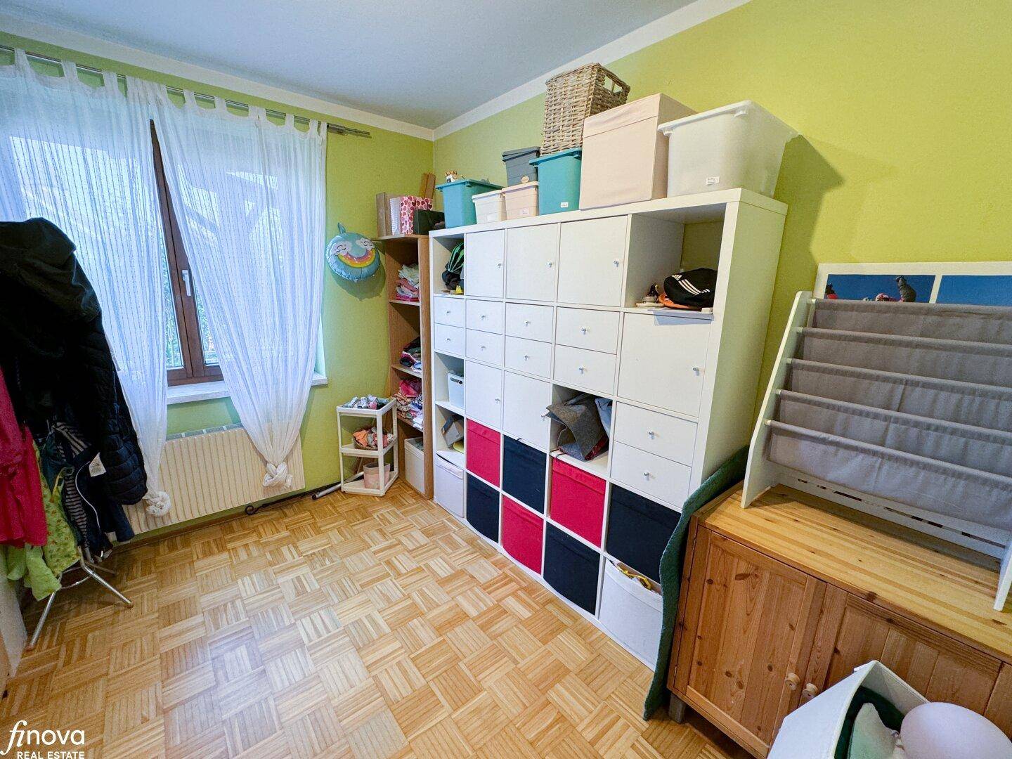 Kinderzimmer mit Stauraumregal, Parkettboden und Fenster, hell und freundlich gestaltet.