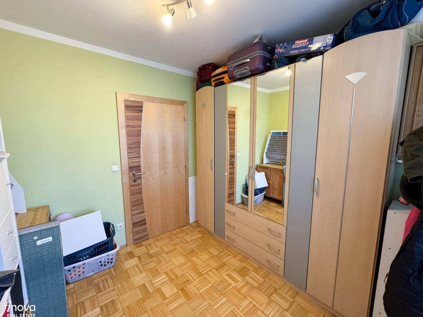 Kinderzimmer mit Kleiderschrank, Parkettboden und grünen Wänden, bietet viel Platz zum Spielen.