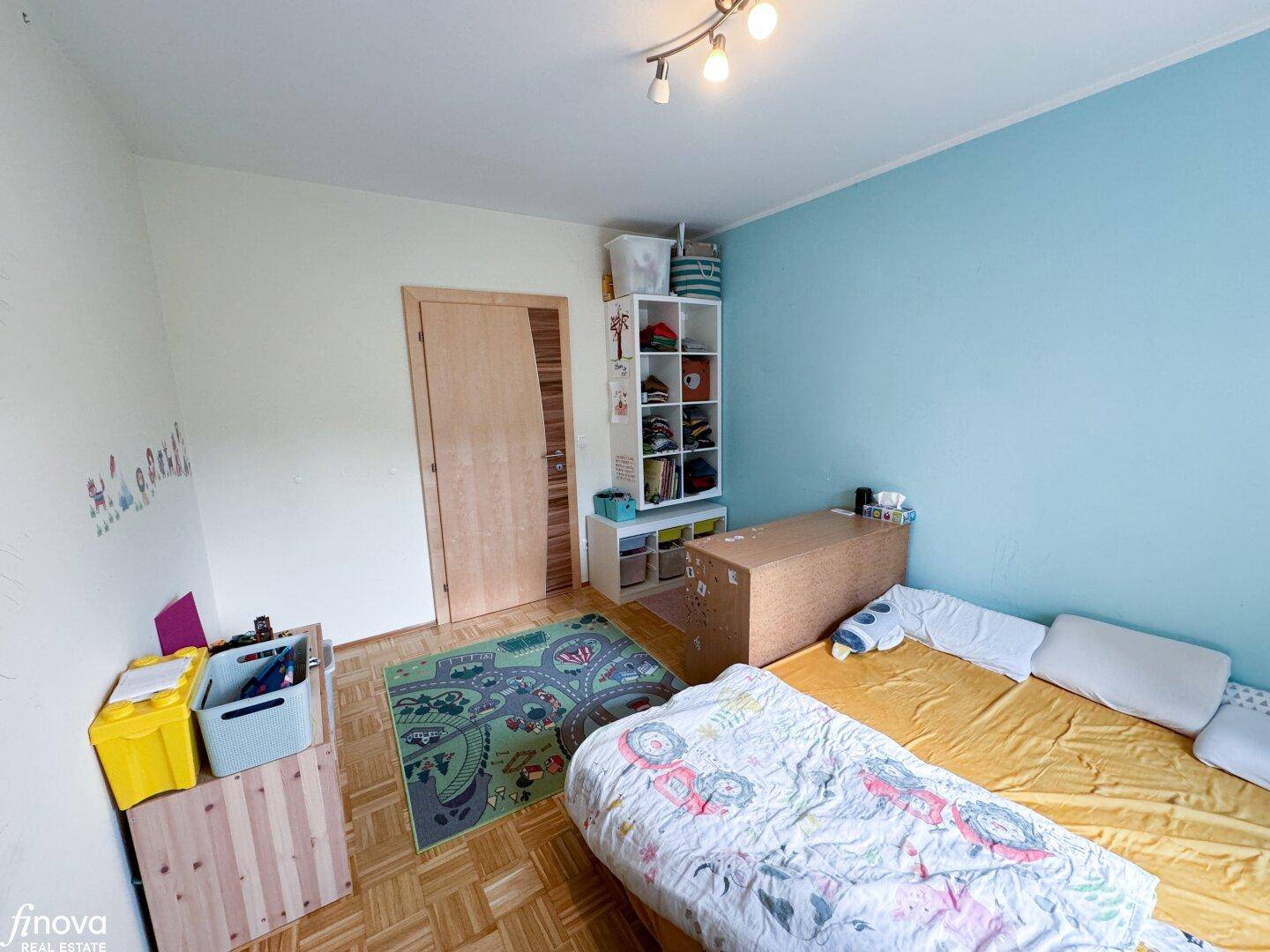 Kinderzimmer mit Einzelbett, Parkettboden und blauer Wand, liebevoll eingerichtet.