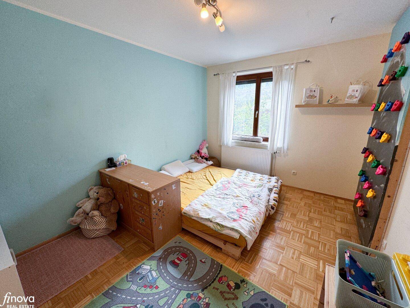Kinderzimmer mit Spielteppich, blauer Wand und Kletterwand, ideal für aktive Kinder.