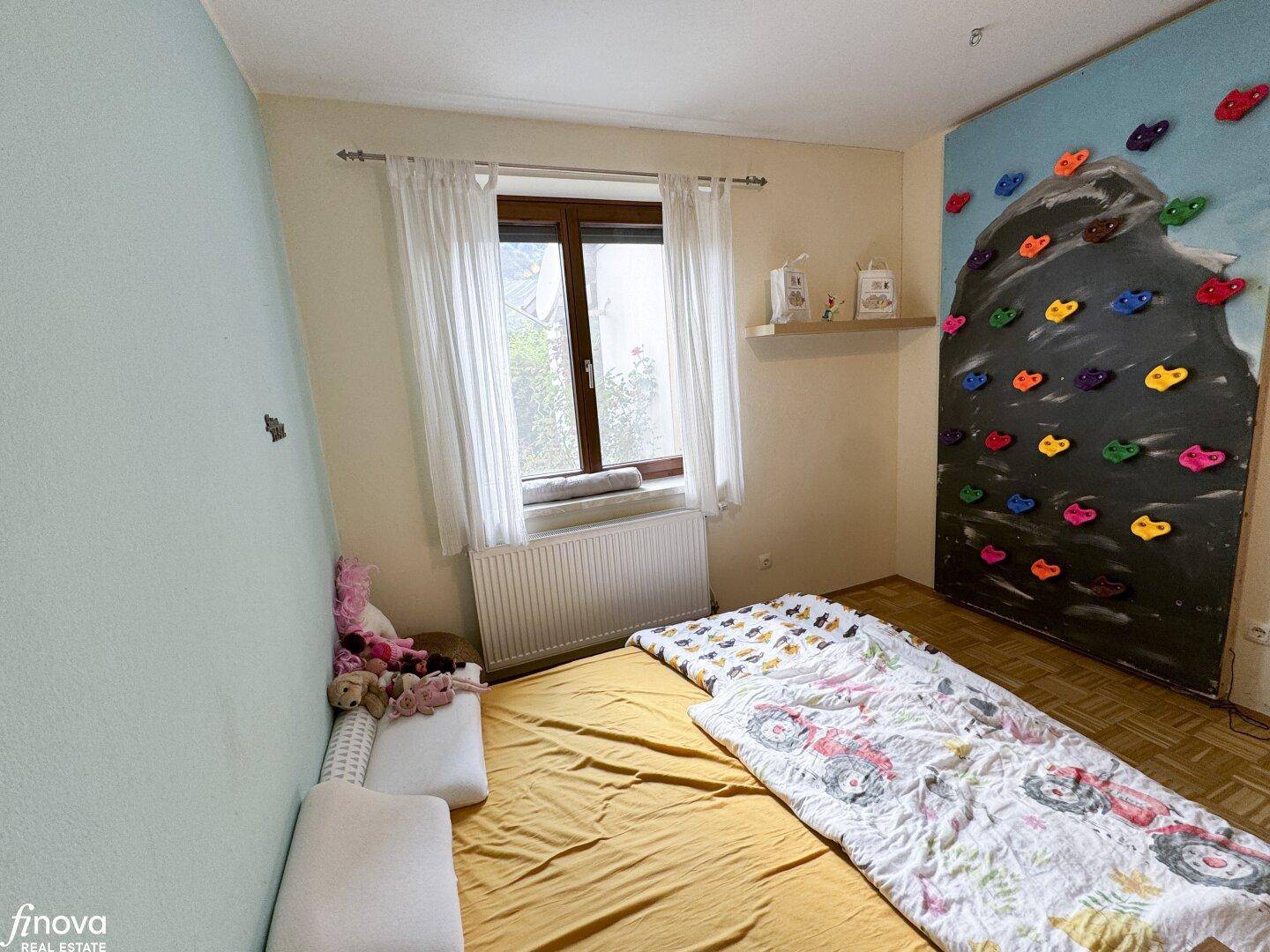 Kinderzimmer mit Fenster, Kletterwand und Spielzeug, bietet eine spielerische Umgebung.
