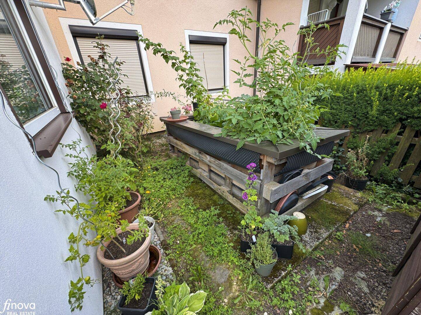 Kleiner Gemüsegarten mit Hochbeet und Topfpflanzen neben dem Haus, ideal für Hobbygärtner.