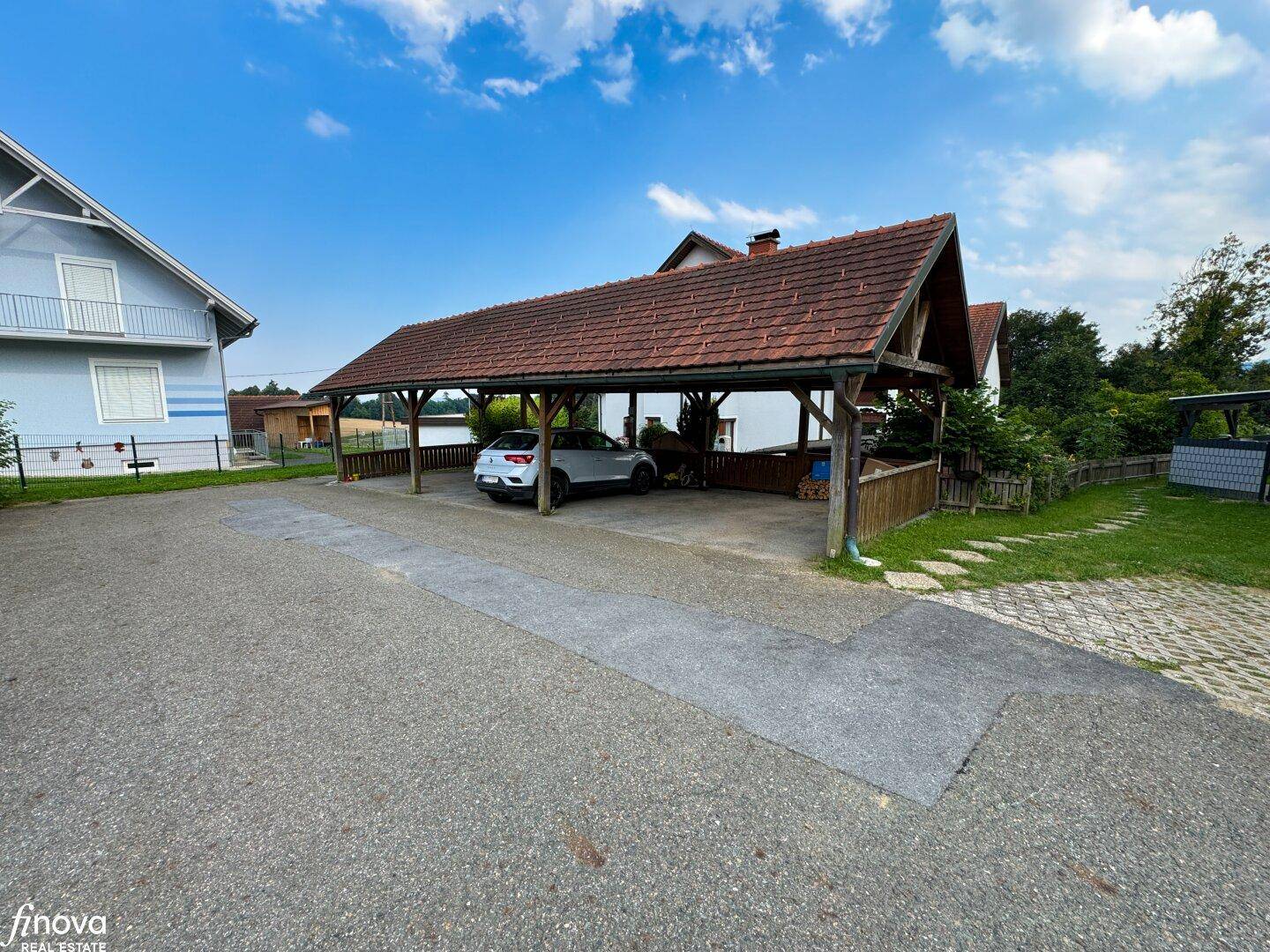 Geräumiger Carport mit Ziegeldach und geparktem Auto auf der Schotterauffahrt.