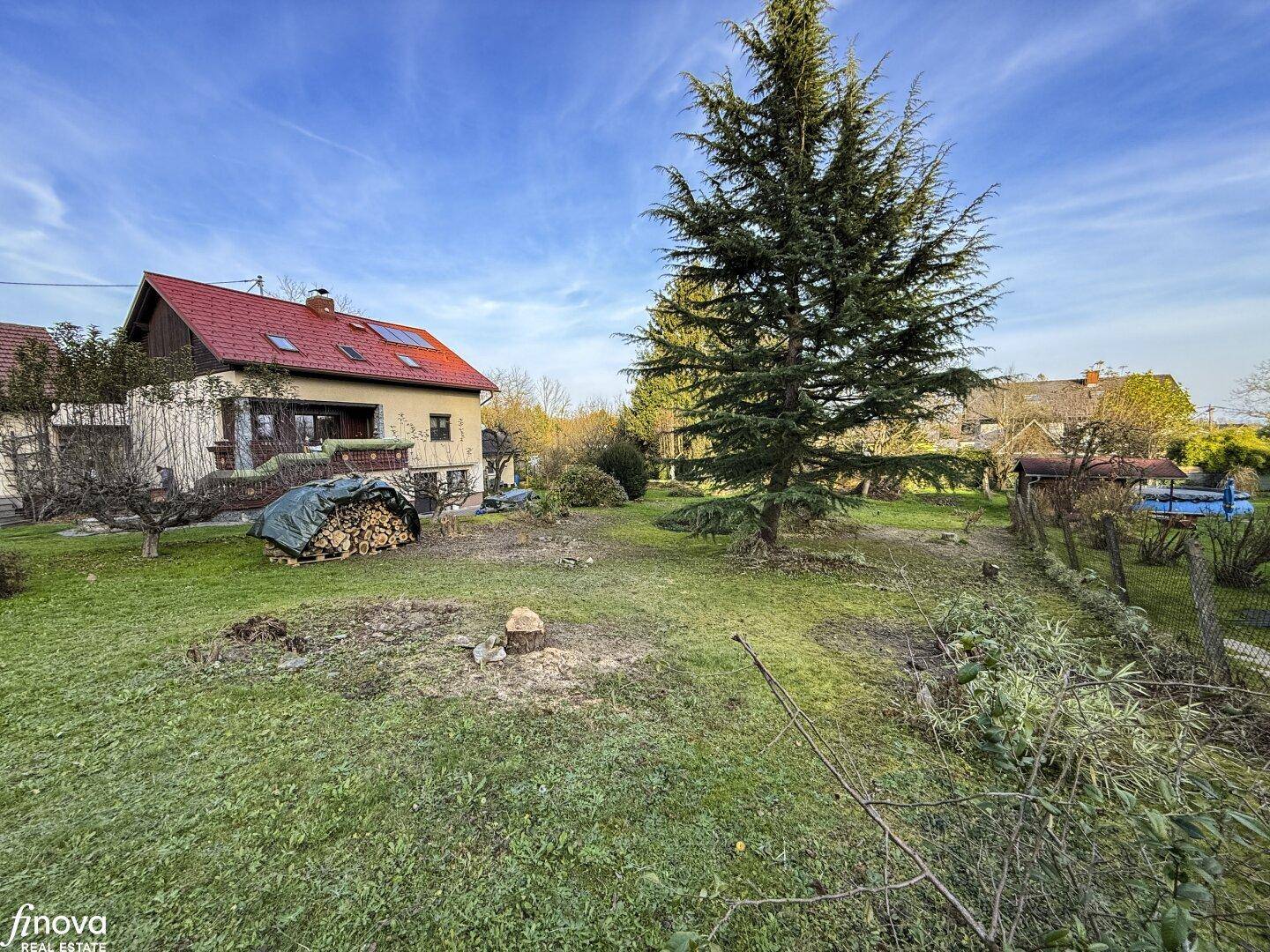 Geräumiger Garten mit Rasen, Baumbestand und einem Haus mit rotem Dach und Solarpaneelen im Hintergrund.