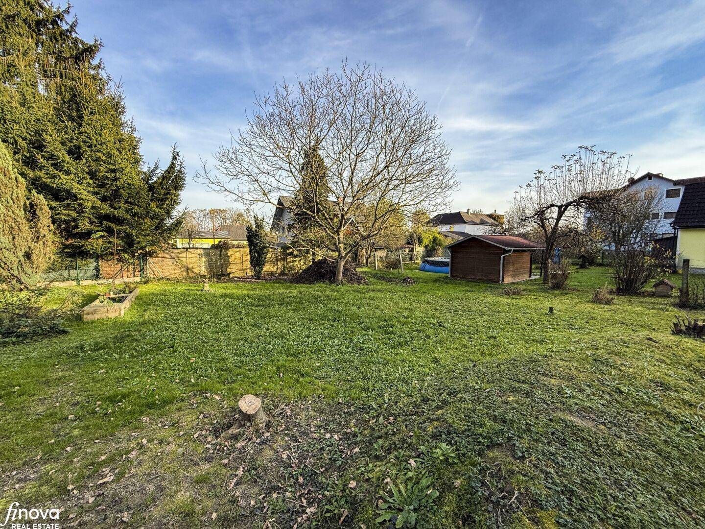 Offener Gartenbereich mit Rasen, einem kleinen Holzschuppen und kahlen Bäumen unter weitem Himmel.