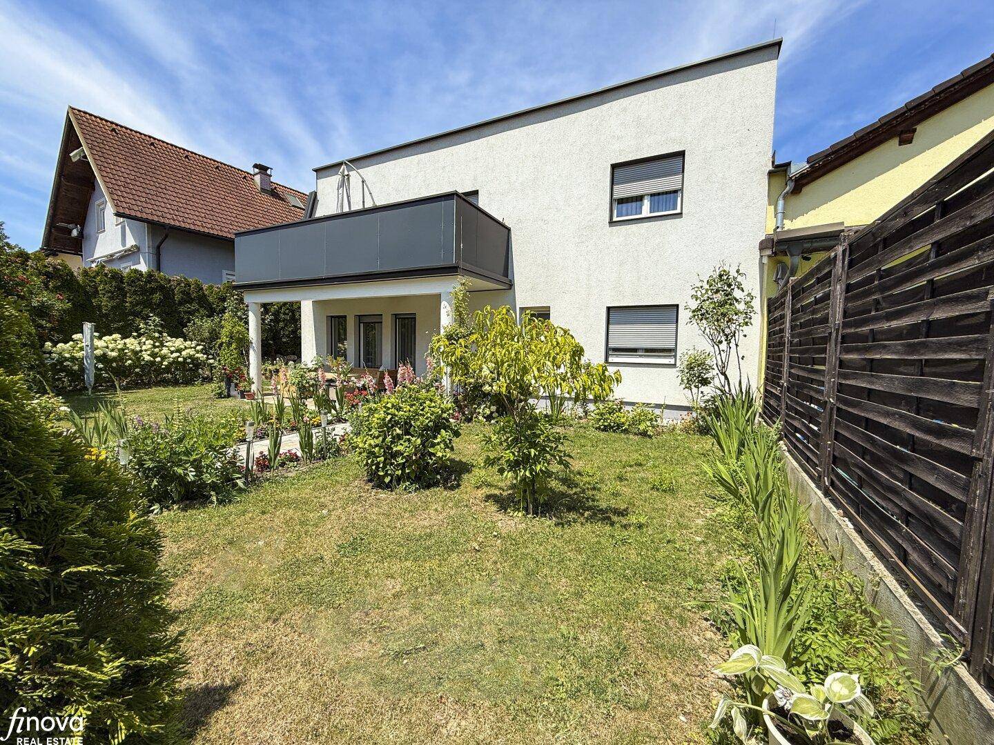 Ansicht des modernen Hauses von der Gartenseite mit Rasenfläche und blühenden Sträuchern.