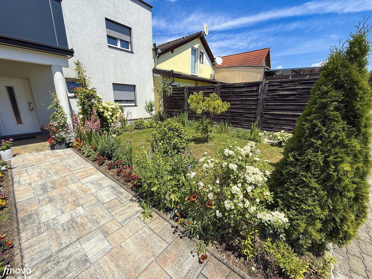 Gepflasterter Eingangsbereich mit bunten Blumenbeeten und einem gepflegten Vorgarten.
