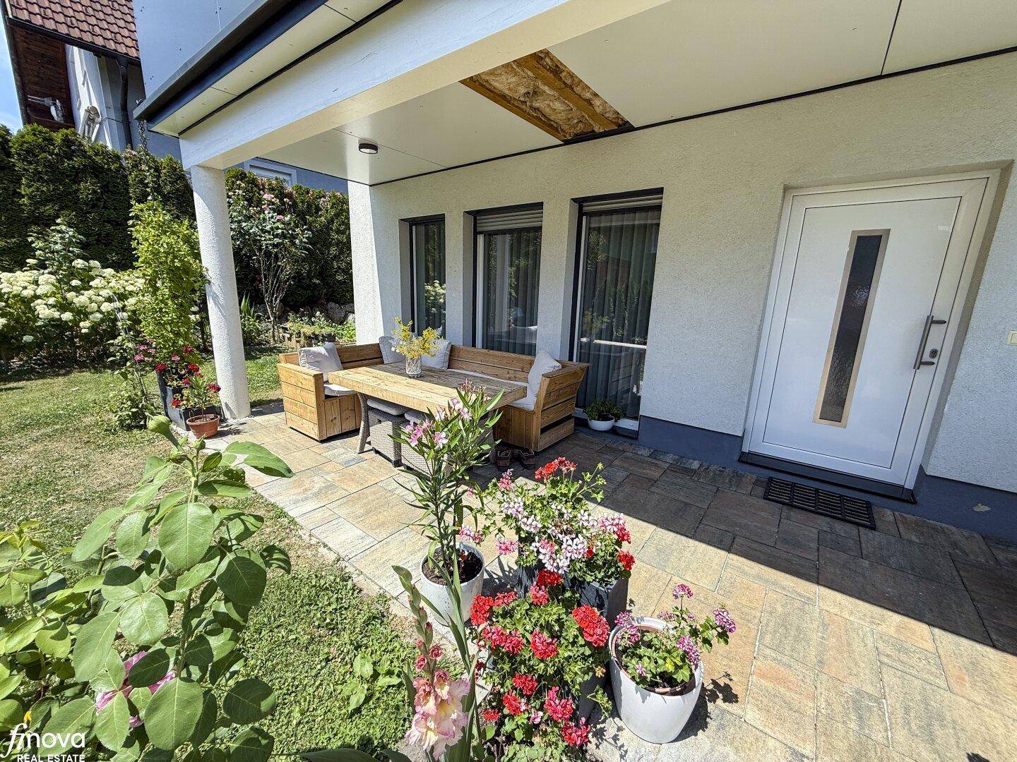 Überdachte Terrasse mit Holzmöbeln und Blumen, direkt am Hauseingang gelegen.