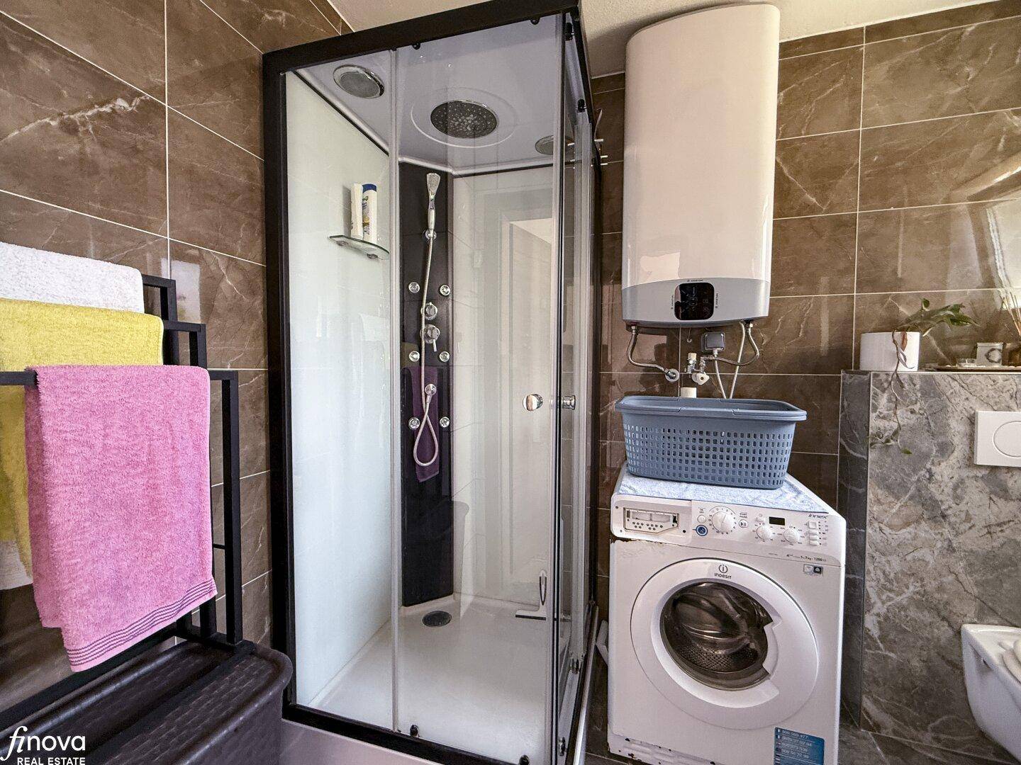 Modernes Badezimmer mit Duschkabine, Waschmaschine und Warmwasserboiler.