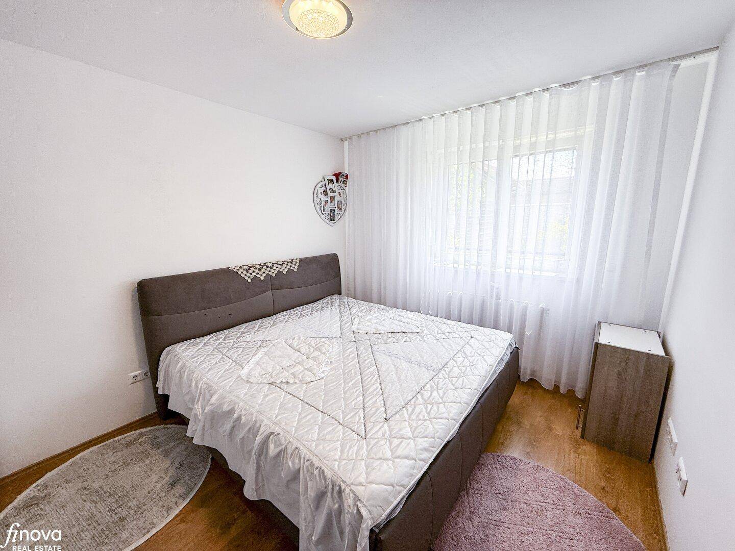 Schlafzimmer mit Doppelbett, Holzboden und einem großen Fenster mit Vorhängen.
