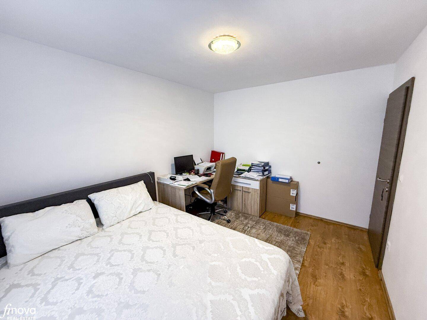 Funktionales Schlafzimmer mit Arbeitsbereich, Holzboden und schlichtem Design.