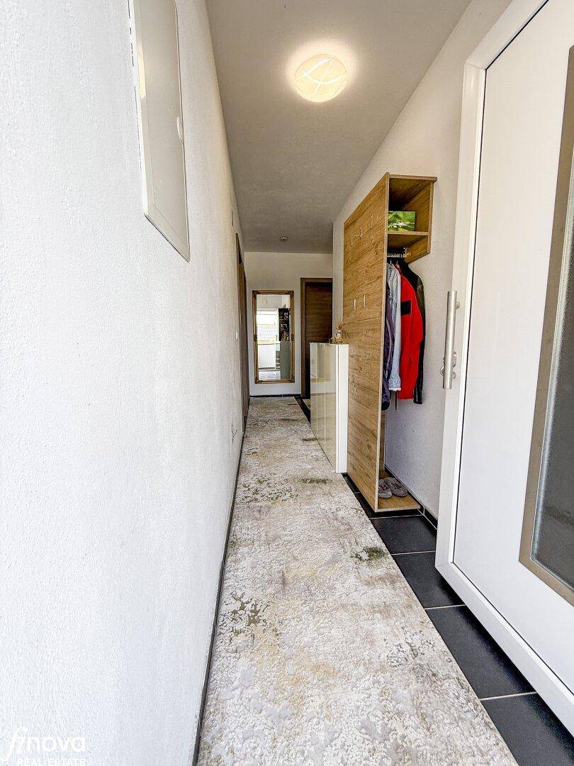 Schmaler Flur mit Teppich, einem kleinen Holzregal und einem Spiegel an der Wand.