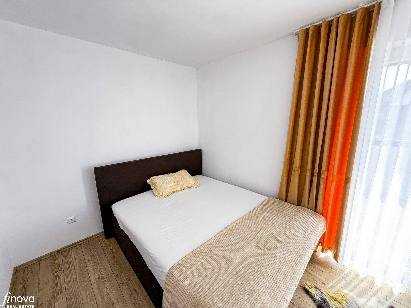 Helles Schlafzimmer mit Einzelbett, Holzboden und farbigen Vorhängen am Fenster.