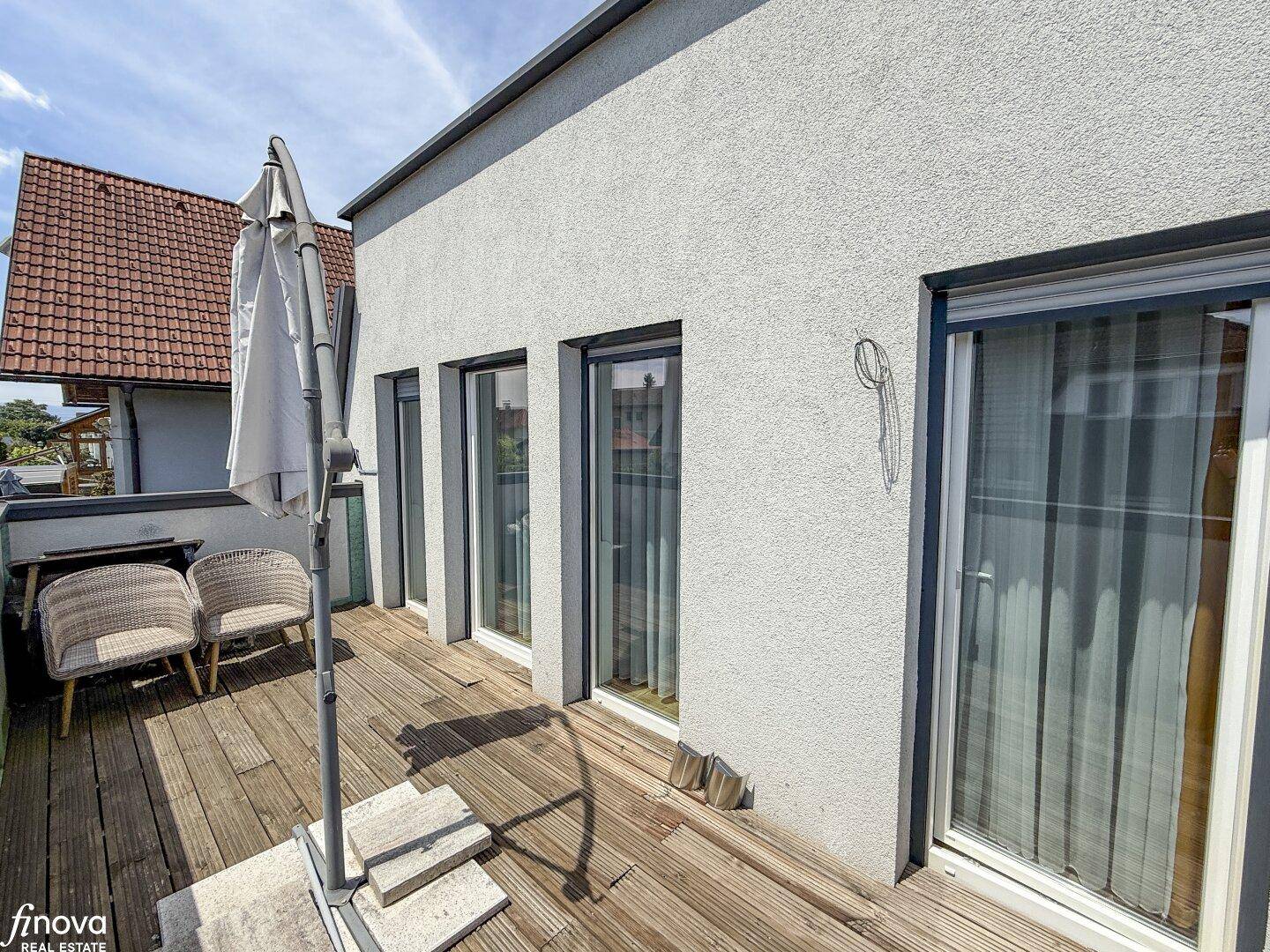 Balkon mit Holzbelag und Zugang zu den Innenräumen durch große Schiebetüren.