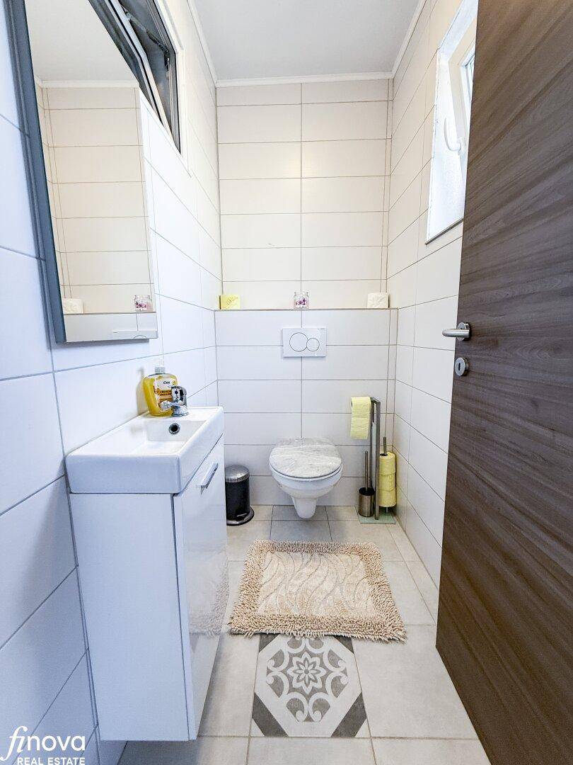Kleines WC mit weißen Wandfliesen, Toilette, Waschbecken und dekorativem Bodenmuster.