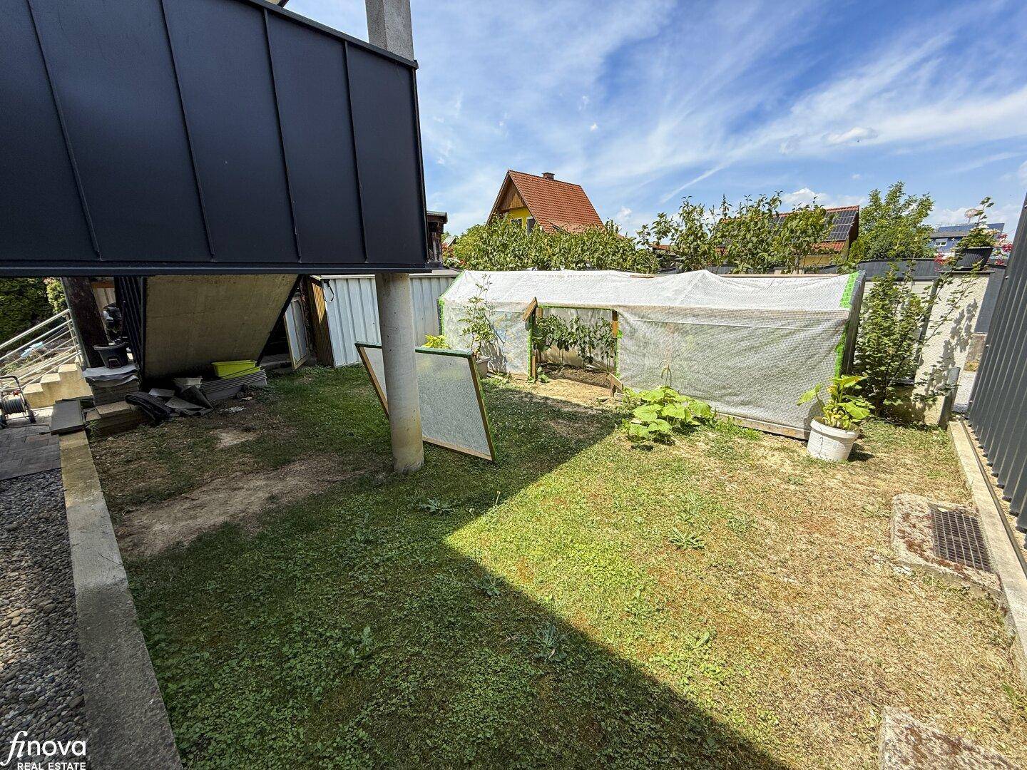 Hinterhofbereich mit Rasenfläche und einem provisorischen Gewächshaus für Pflanzen.