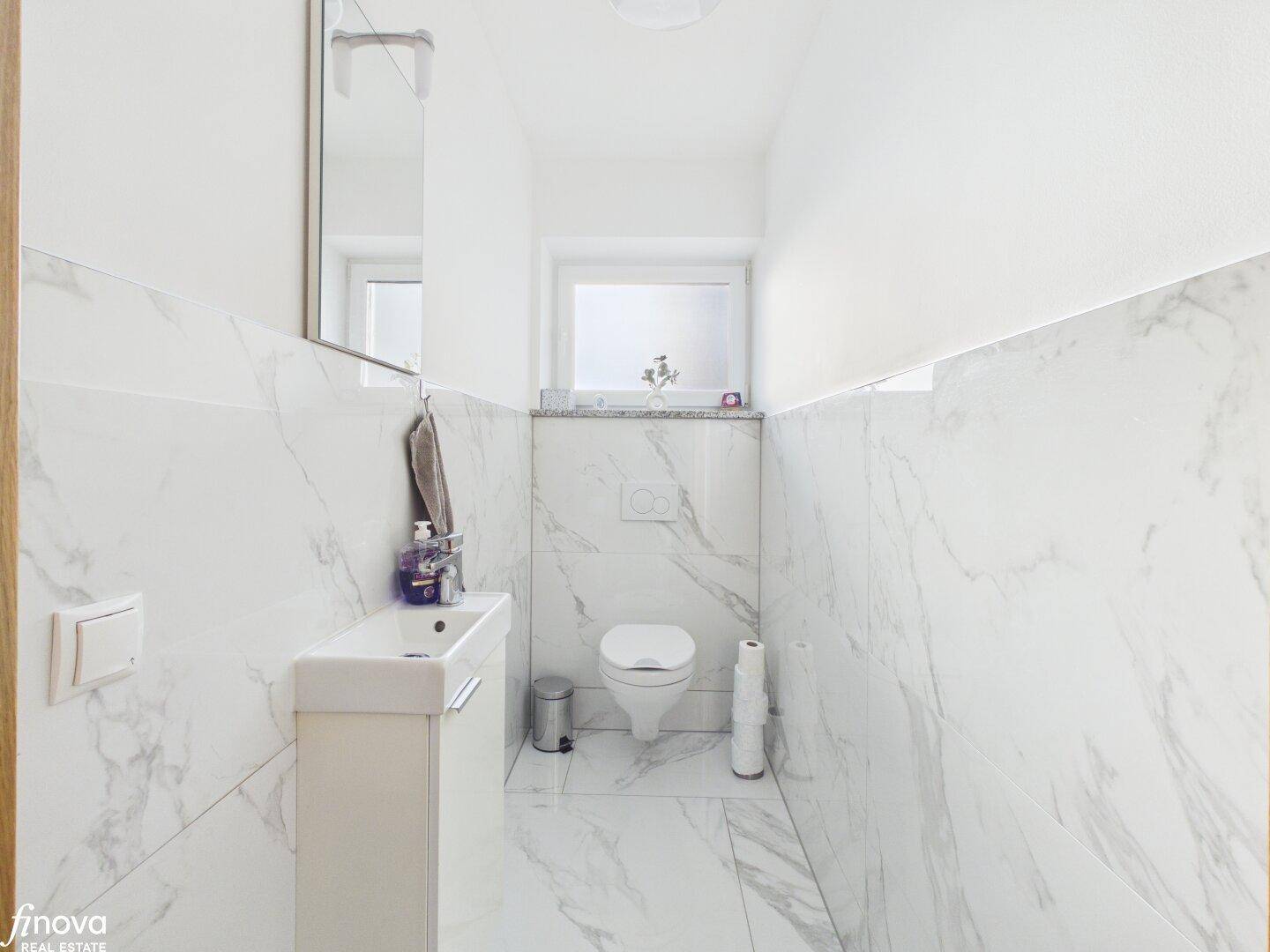 Modernes Gäste-WC mit Marmorfliesen, wandhängendem WC und kleinem Waschbecken.