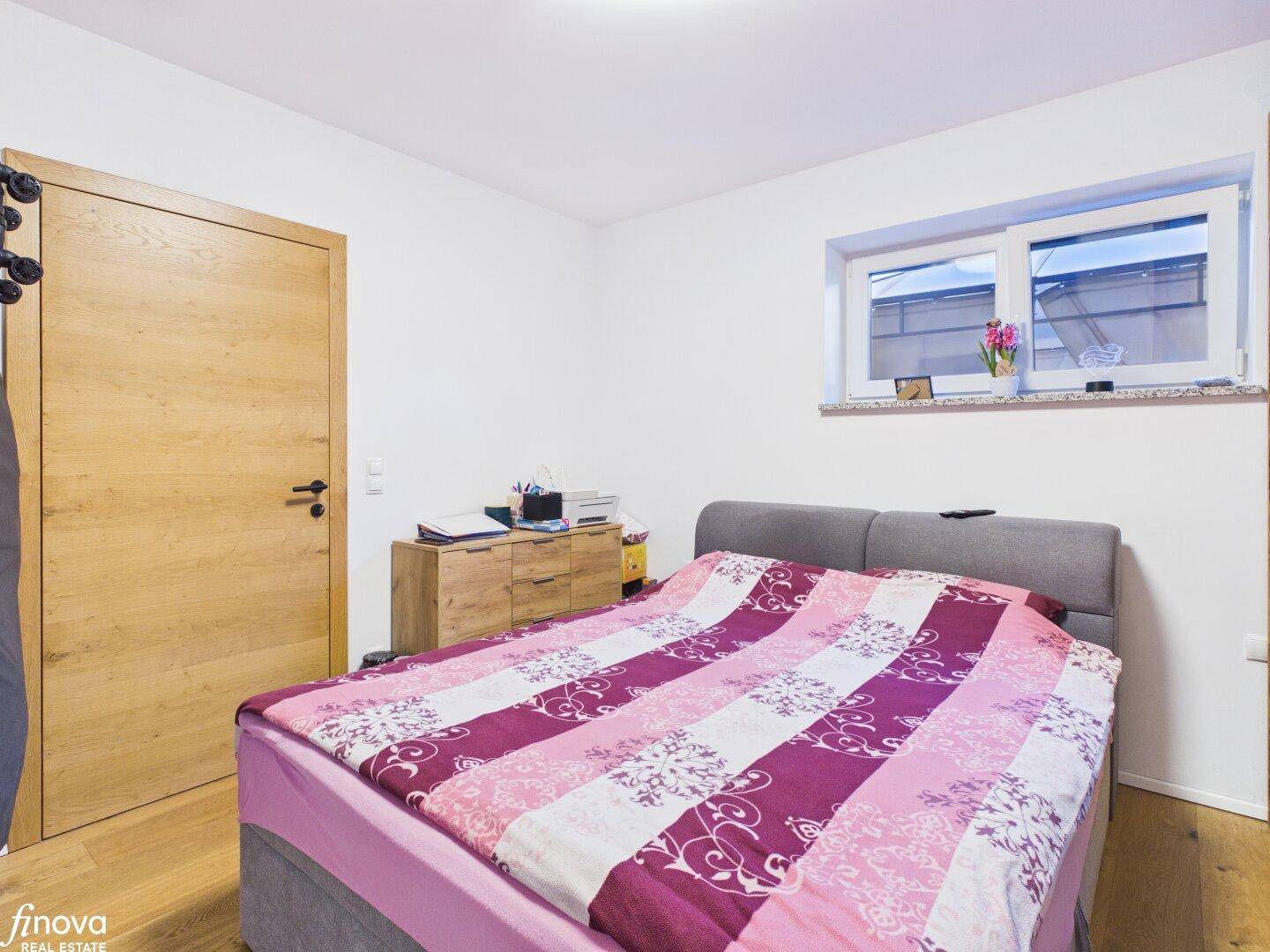 Schlafzimmer mit Holzboden, Holztür und Fenster für natürliches Licht.