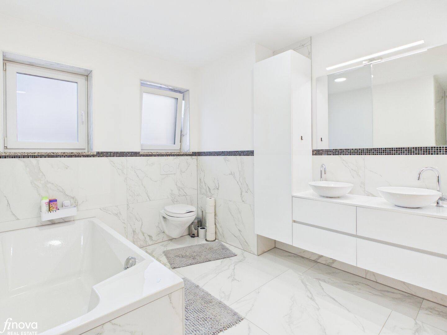 Helles Badezimmer mit Doppelwaschbecken, Badewanne und großem Spiegel.