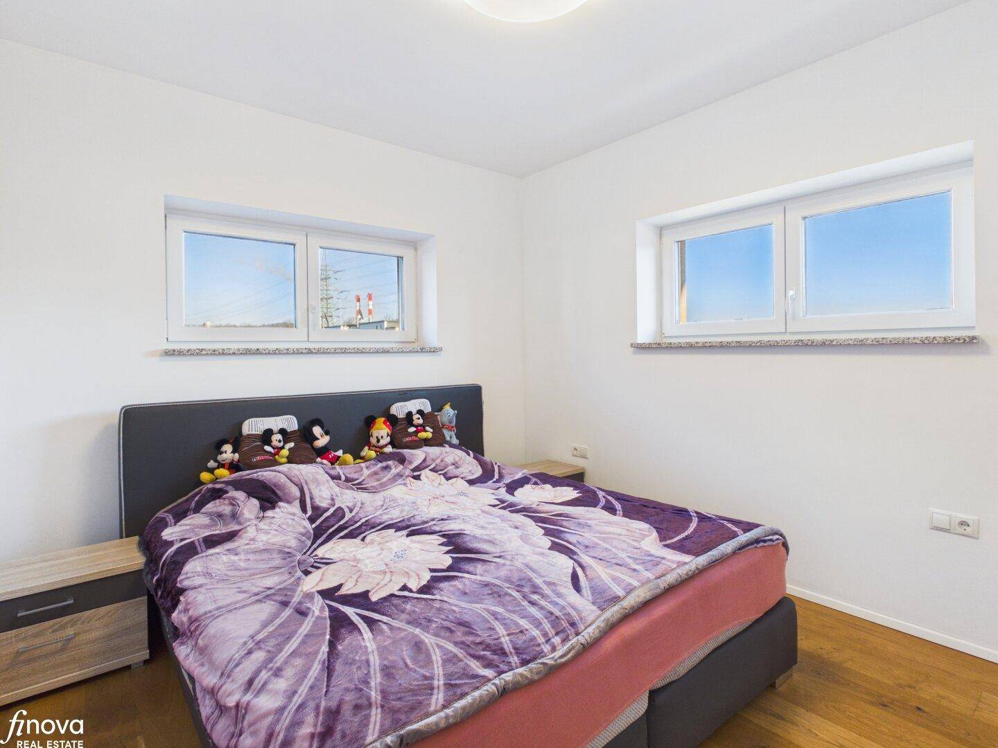 Schlafzimmer mit Holzboden und zwei Fenstern für gute Belichtung.