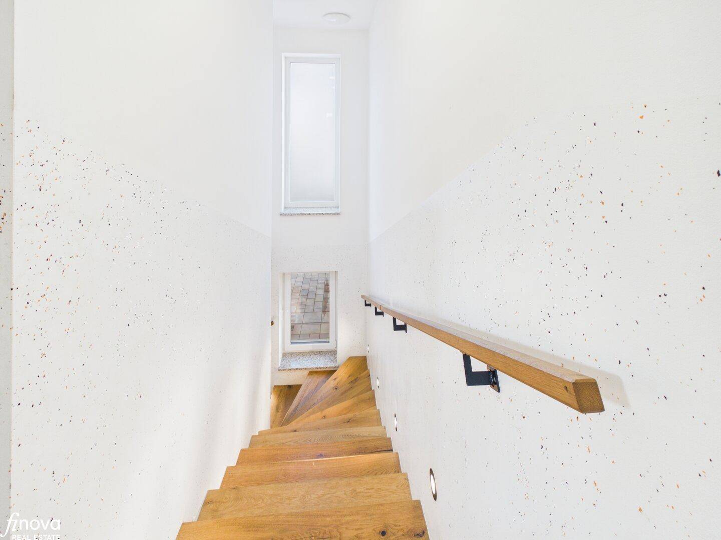 Heller Treppenaufgang mit Holzstufen und schmalen Fenstern für Tageslicht.