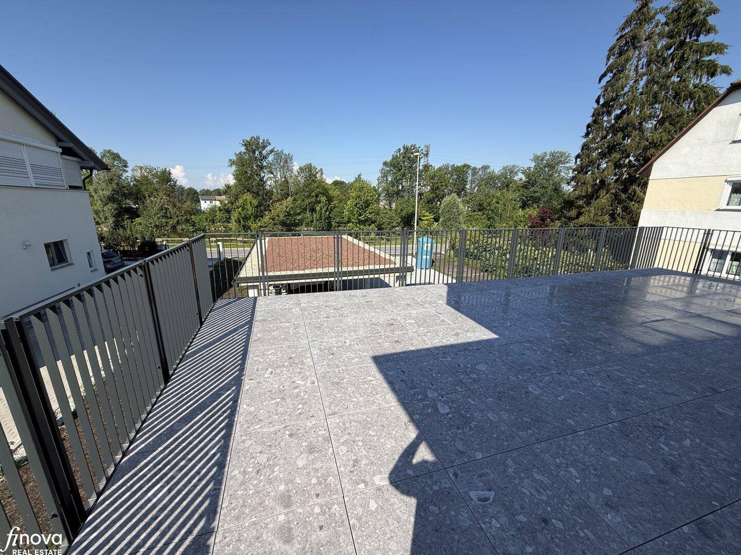 Weitläufige Terrasse mit Blick auf die grüne Umgebung und angrenzende Gebäude.