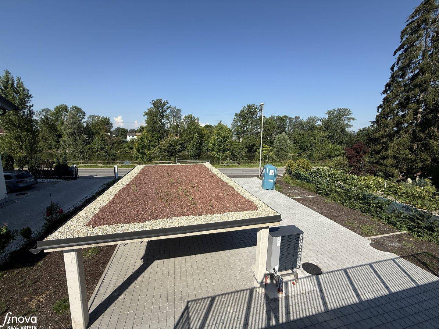 Moderner Carport mit begrüntem Dach und gepflasterter Zufahrt, umgeben von viel Grün.