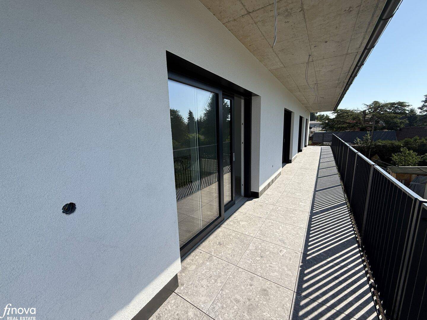 Langer Balkon mit modernen Fliesen und schwarzem Geländer, bietet Zugang zu mehreren Räumen.