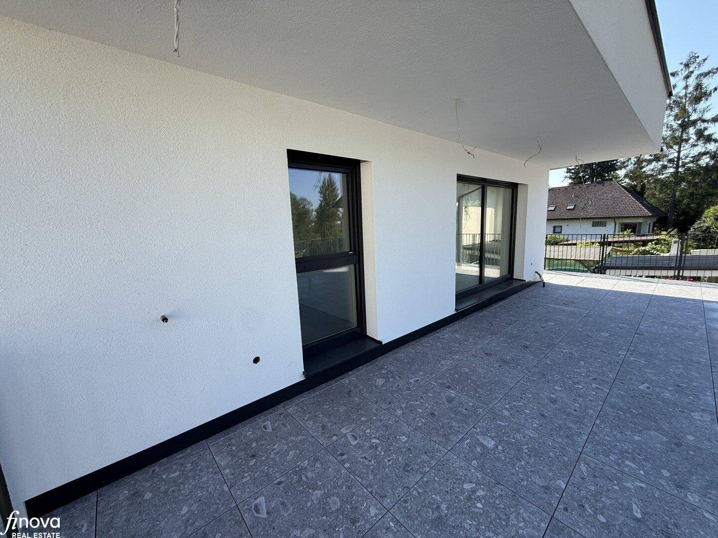 Detailansicht der gefliesten Terrasse mit großen Fenstern und weißer Fassade.