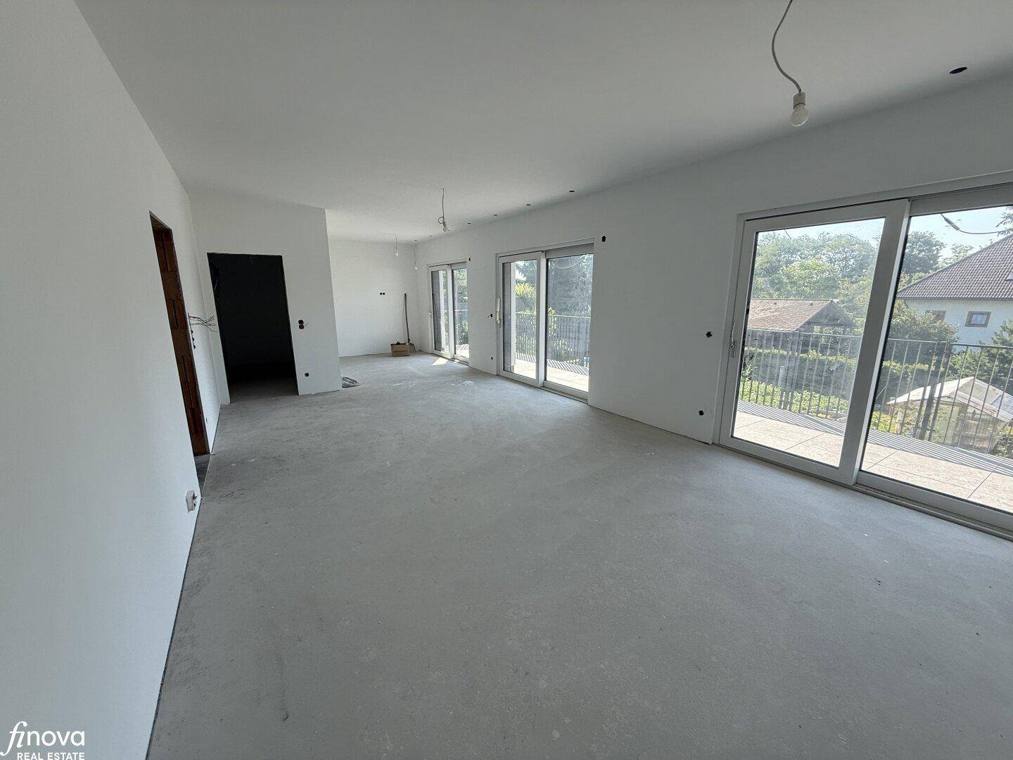 Geräumiger Wohnbereich im Rohbau mit großen Schiebetüren zur Terrasse und viel Tageslicht.